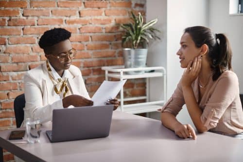African American human resource manager talking to job candidate while reading her CV during a meeting in the office.
