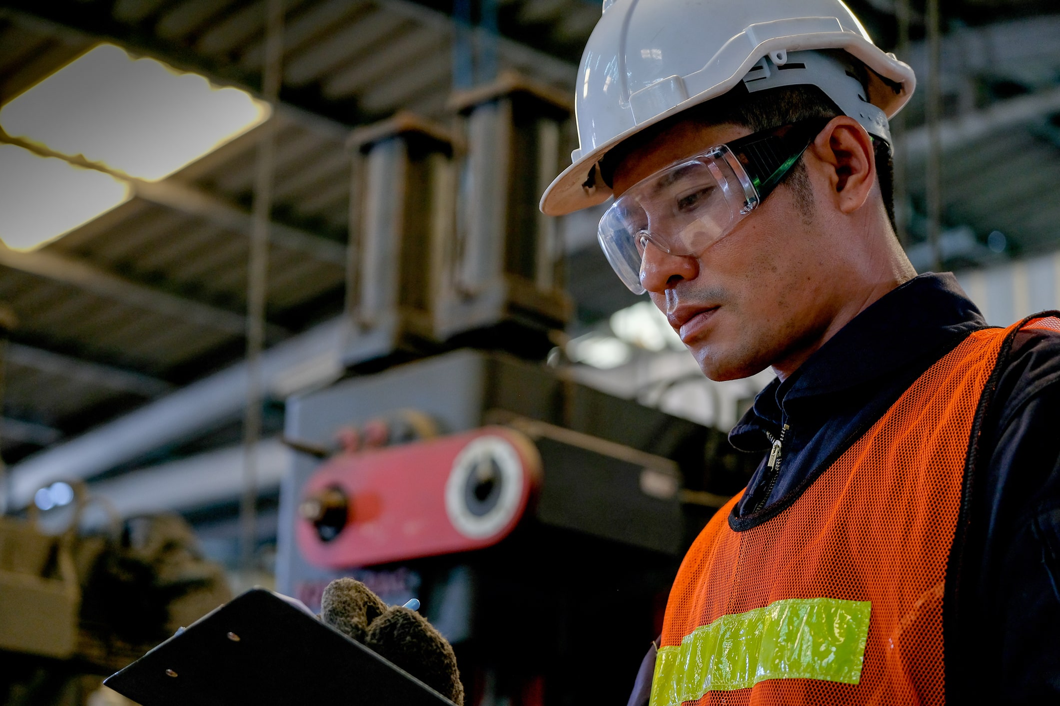 Close up Asian worker or technician man write on document paper in factory in front of machine.