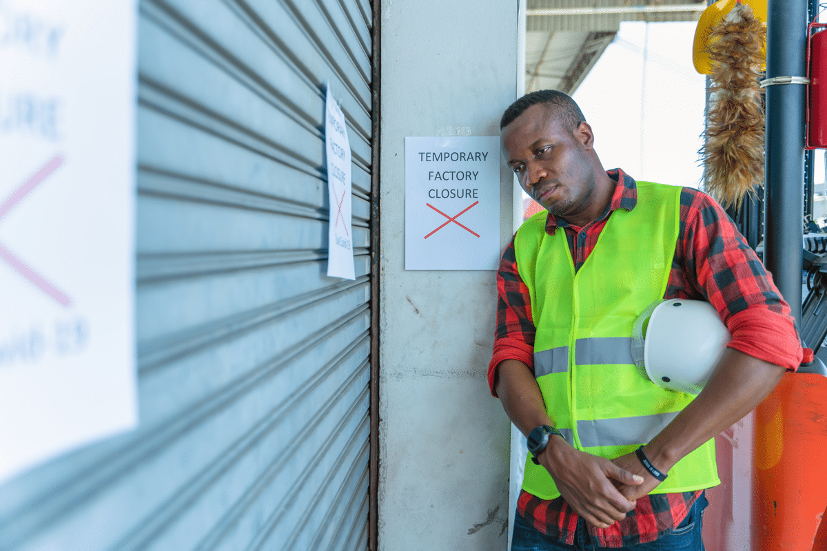 man standing next to 'factory closed' sign