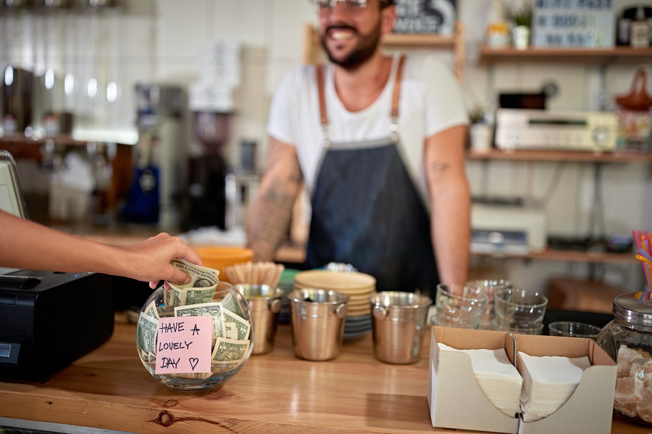 satisfied customer in coffee shop leaving tip in a bowl with a positive message on a sticker. money, tip, satisfied, positive message