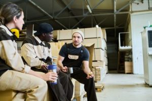 Group of manual workers in uniform talking to each other during coffee break at warehouse