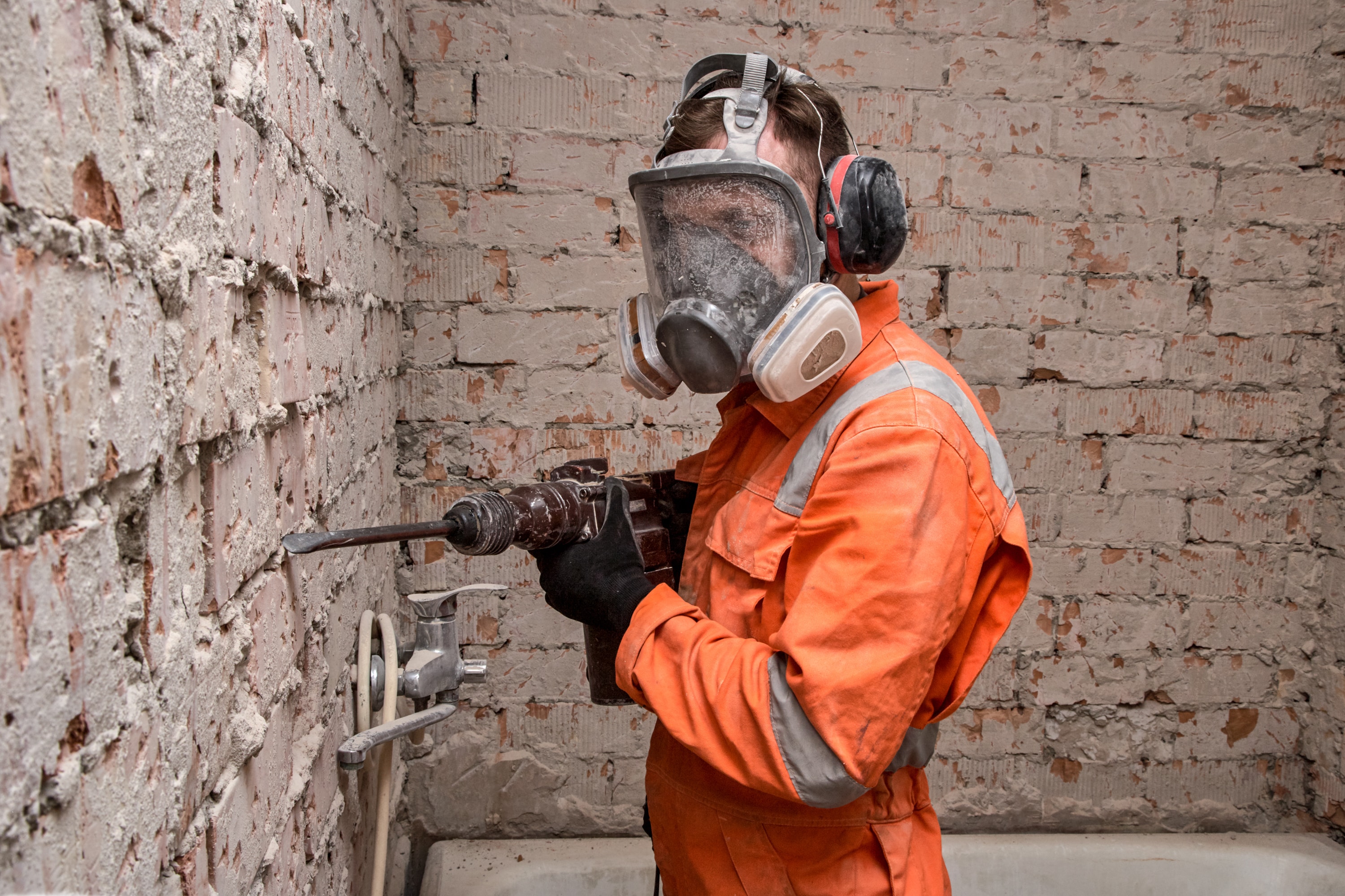 Construction worker wearing full face respirator mask and ear defenders for working with hammer drill.