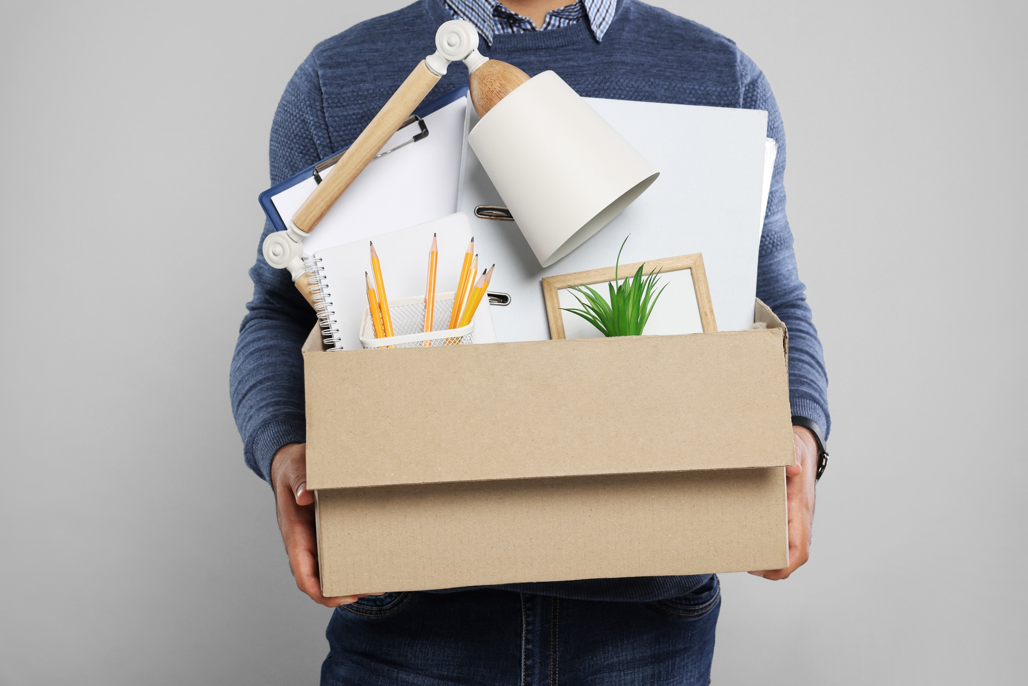 man with box of personal office belongings on light grey background, closeup