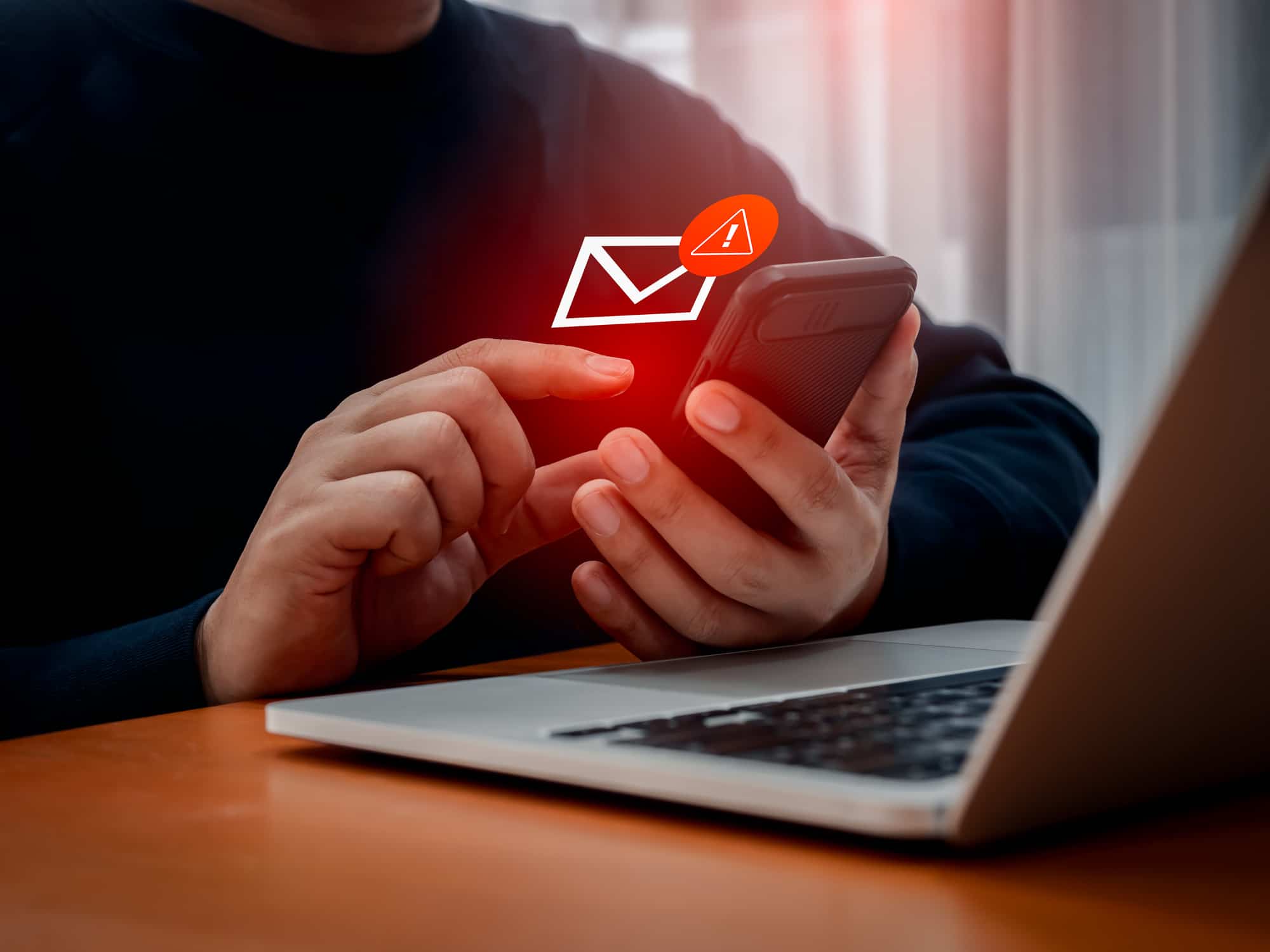 person getting alarming email on phone, sitting at laptop