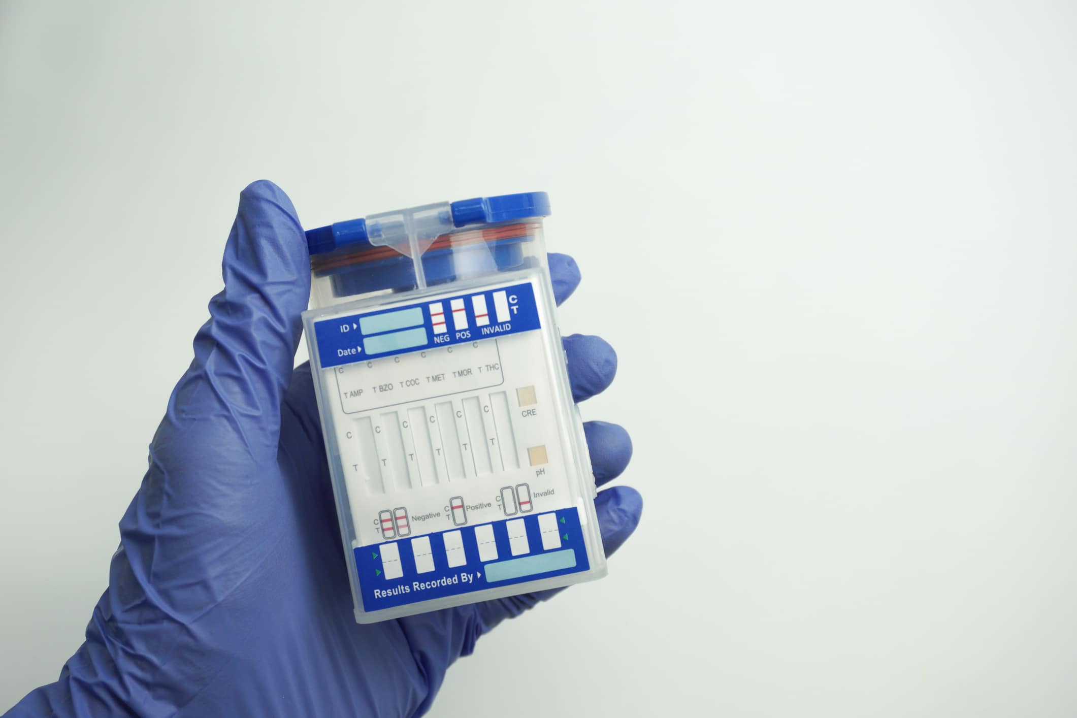 Hand in blue glove holding an empty container for analysis. Drug test concept. Isolated on white background.