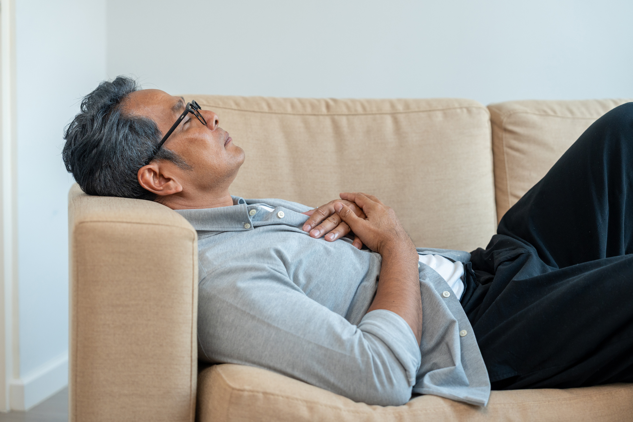 Mature Asian caucasian man lying on comfortable sofa in living room. 