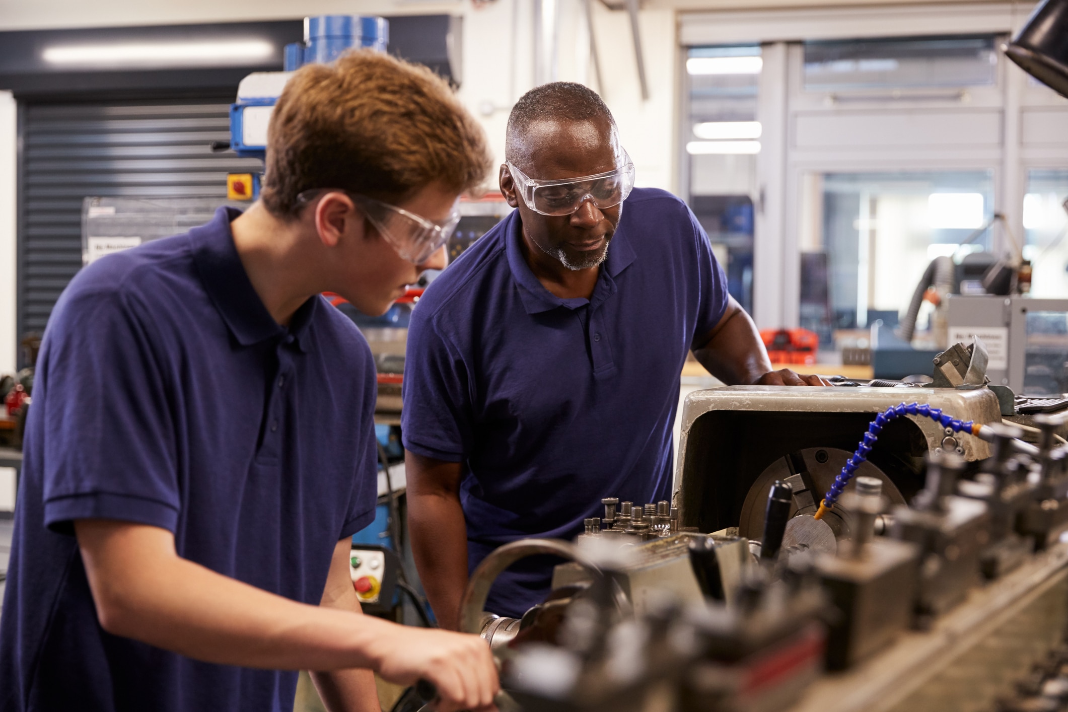 Engineer Showing Teenage Apprentice How To Use Lathe
