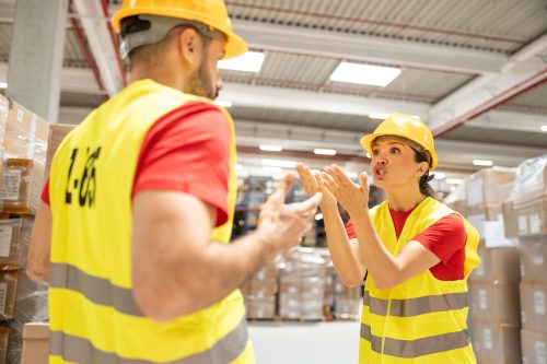 Two warehouse workers in a dispute, showcasing emotions and communication in a hectic warehouse environment.